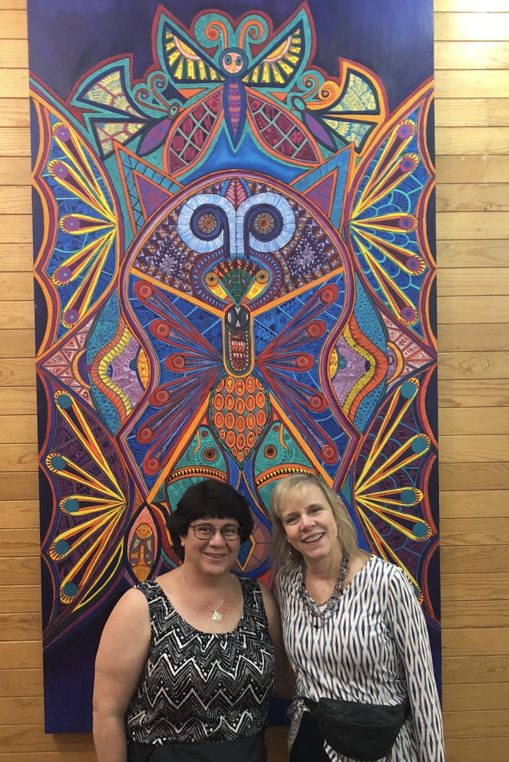 Cara and Erin pose together in front of a large colorful painting while at a wellness event in Mexico