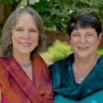 Erin and Cara stand together outside under a tree and smile at the camera